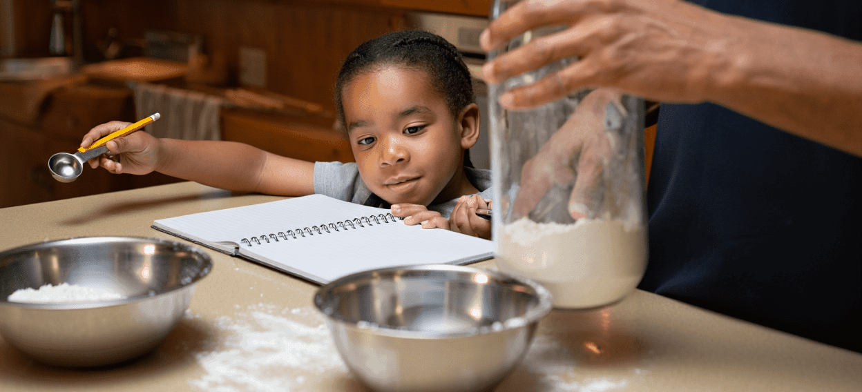 Child and adult baking, with flour, bowls, and a notebook on the counter.